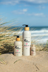 Three bottles of Rad Spa shower gel on a sandy beach with ocean and sky in the background