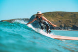 Rad Wax Ambassador surfing on a wave with a clear blue sky and green landscape in the background